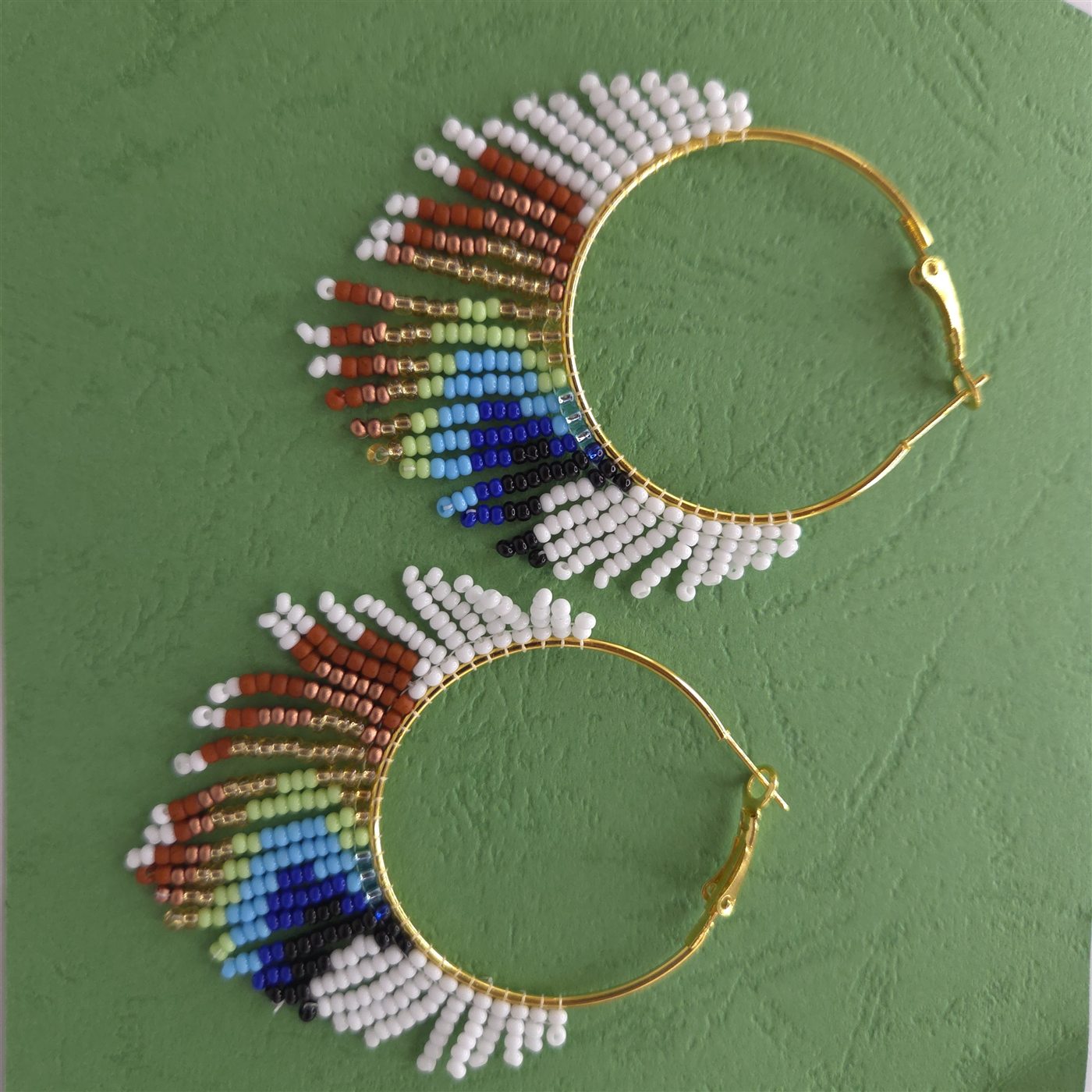 Gold hoop earrings with rainbow handmade beadwork on a green background